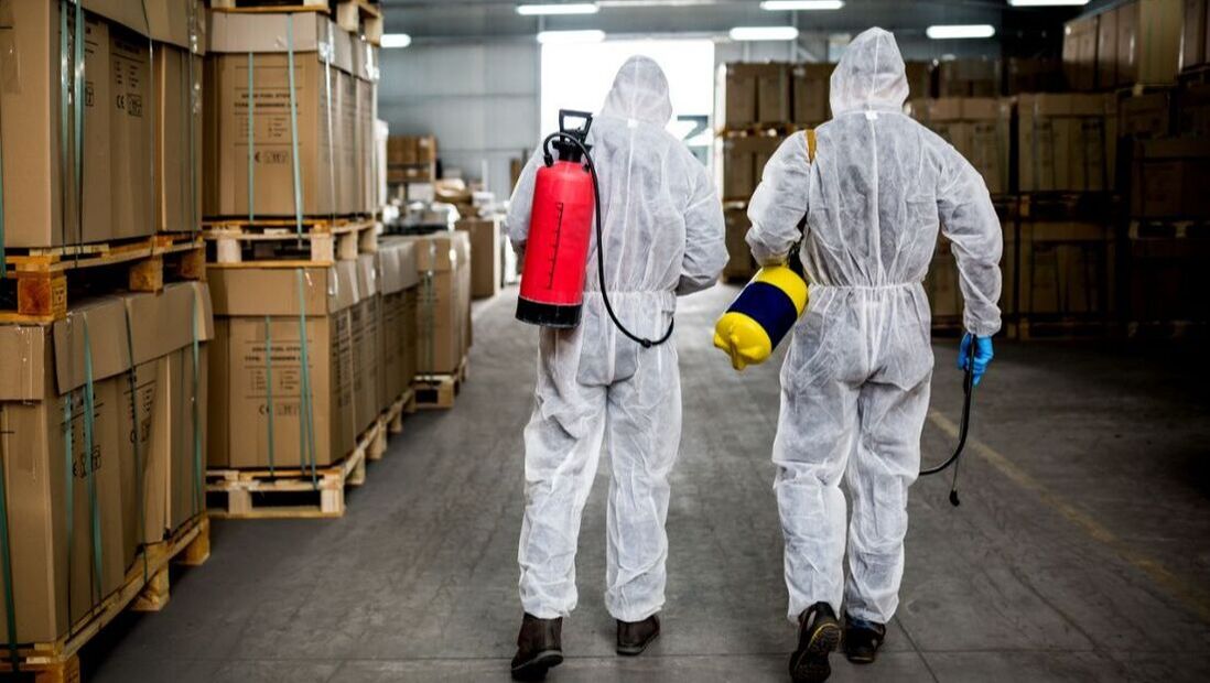 Two pest control professionals with sprayers inside an industrial warehouse in Penang